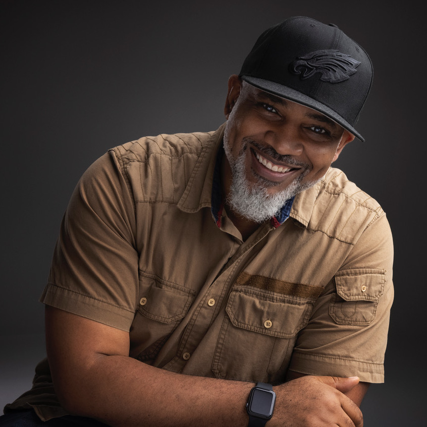 Will Ragland headshot Man with hat and a beard smiling with his arm across his body
